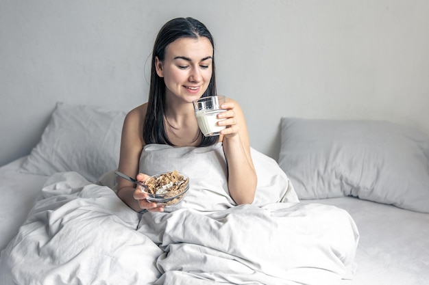 Una mujer joven en una cama blanca con cereales y leche.