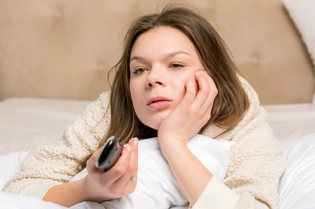 Foto mujer joven en la cama con control remoto