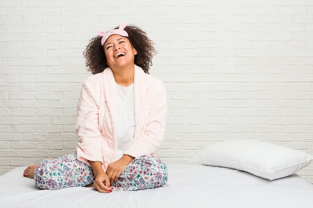 Mujer joven en la cama con pijama relajado y feliz riendo, cuello estirado mostrando dientes