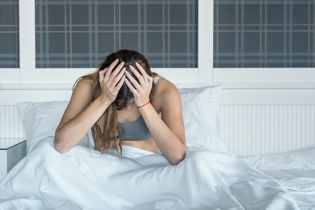 Mujer joven en la cama solo se despierta con un dolor de cabeza