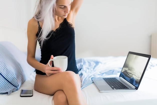 mujer joven, en cama, con, taza de café, y, computador portatil