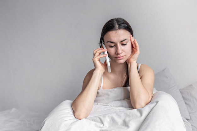 Una mujer joven en la cama con un teléfono inteligente por la mañana