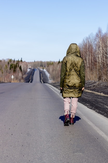 Una mujer joven camina al lado de la carretera. Camino en el bosque.