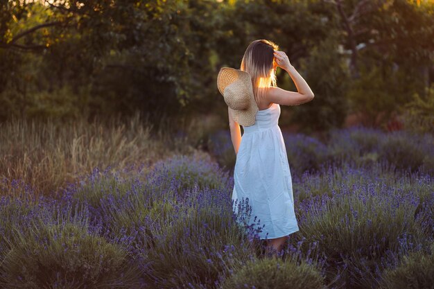 Mujer joven camina fuera de la ciudad entre la niña lavanda se para al atardecer en el prado y mira hacia atrás