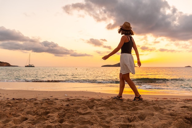 Mujer joven caminando al atardecer en la playa de Cala Comte en la isla de Ibiza Balearic