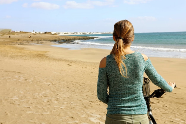 Mujer joven caminando con bicicleta en la playa salvaje