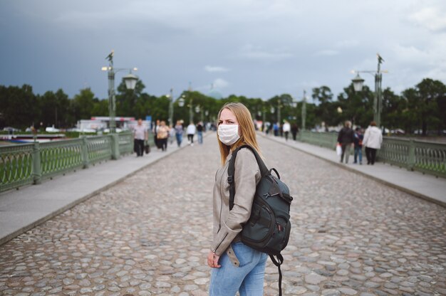 Mujer joven caminando en las calles de la ciudad entre la multitud con mochila con máscara protectora para la prevención de Covid 19