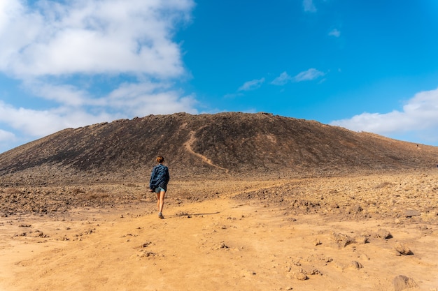 Una mujer joven caminando por el camino hacia el cráter del volcán Calderón Hondo cerca de Corralejo, costa norte de la isla de Fuerteventura, Islas Canarias. España