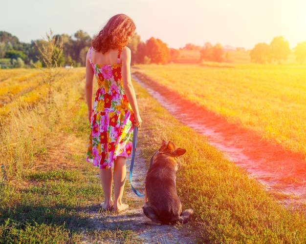 Mujer joven caminando descalzo con perro en camino rural a la cámara.