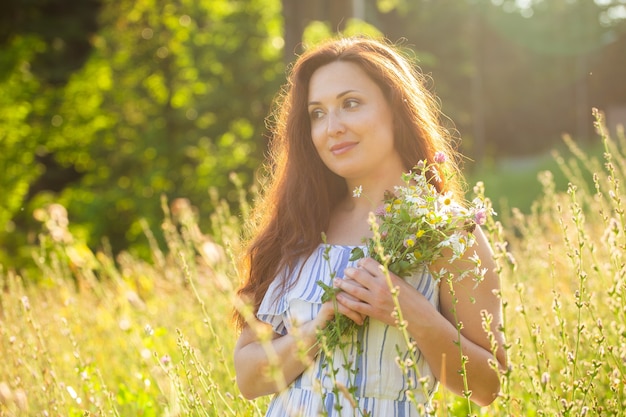 Mujer joven caminando entre flores silvestres en un día soleado de verano concepto de la alegría de comunicarse con