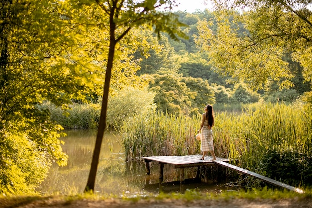 Mujer joven caminando en el muelle de madera en el lago tranquilo en un caluroso día de verano