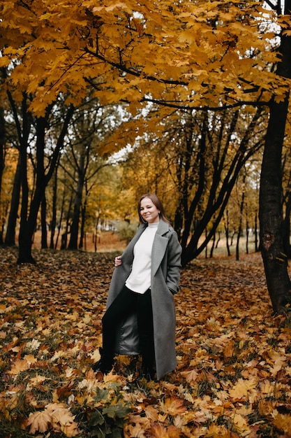 Mujer joven caminando en el parque de otoño con un abrigo largo