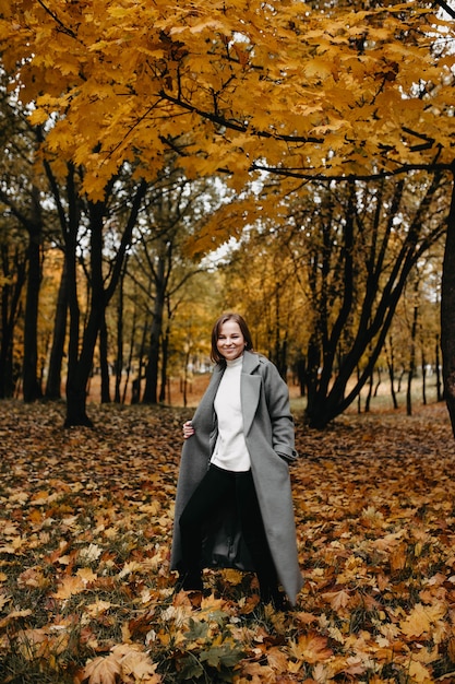 Mujer joven caminando en el parque de otoño con un abrigo largo
