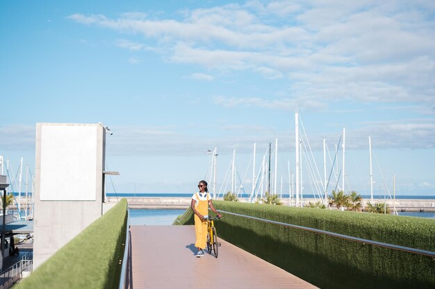 Mujer joven caminando por el paseo con su bicicleta amarilla Concept estilo de vida al aire libre colores