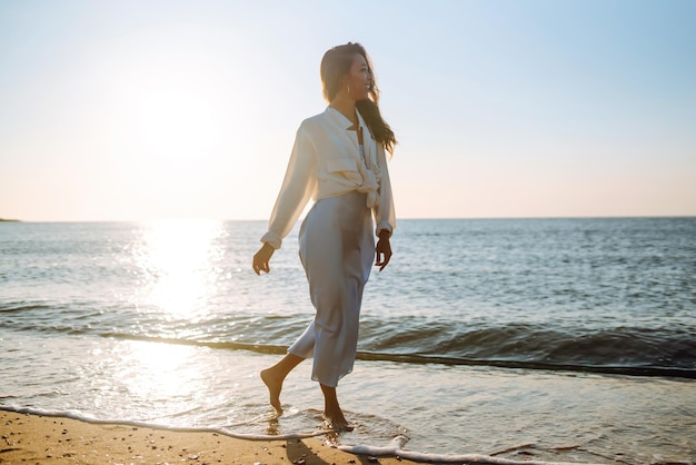 Mujer joven caminando en la puesta de sol en la playa Horario de verano Concepto de estilo de vida de fin de semana de viaje