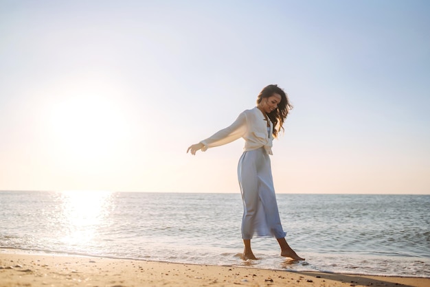 Mujer joven caminando en la puesta de sol en la playa Horario de verano Concepto de estilo de vida de fin de semana de viaje