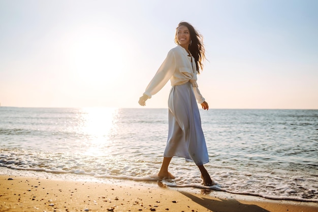 Mujer joven caminando en la puesta de sol en la playa Horario de verano Concepto de estilo de vida de fin de semana de viaje