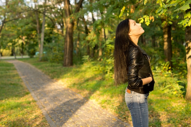 Mujer joven en un camino del parque mirando árboles.