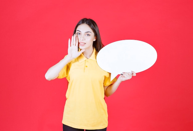 Mujer joven con camisa amarilla sosteniendo un tablero de información ovale e informando a todos sobre el proyecto