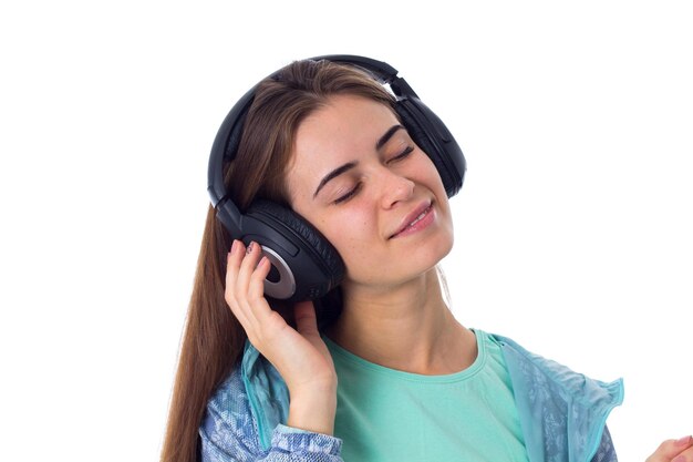 Mujer joven en camisa azul escuchando música en auriculares negros sobre fondo blanco en estudio