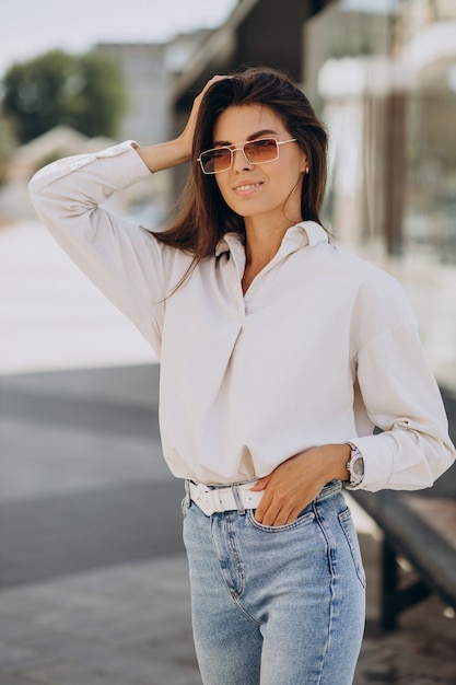 Foto mujer joven con camisa blanca caminando fuera de las calles de verano