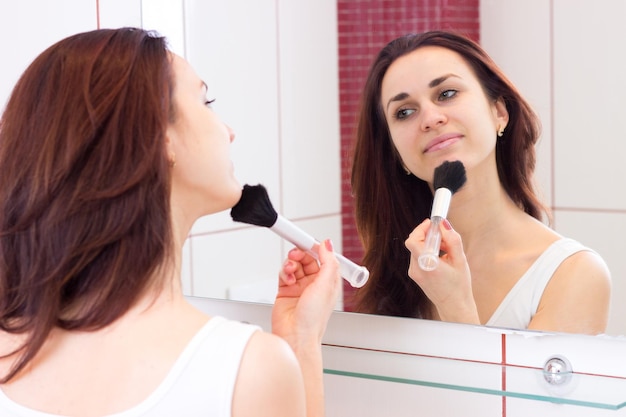 Mujer joven con camisa blanca pulverizándose con cepillo frente al espejo en su baño burdeos