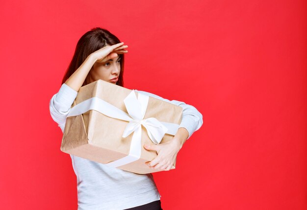 Mujer joven con camisa blanca sosteniendo una caja de regalo de cartón