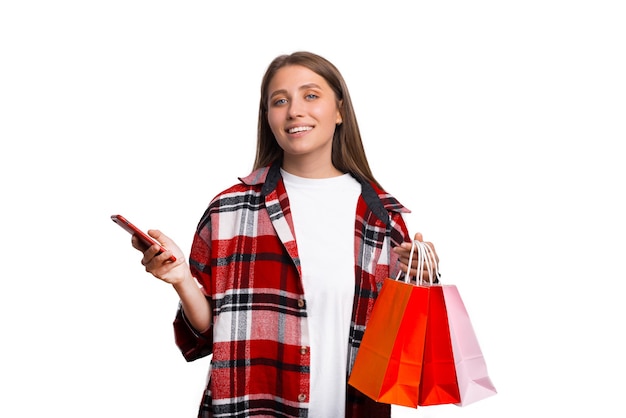 Mujer joven con camisa a cuadros está sosteniendo algunas bolsas de la compra y su teléfono.