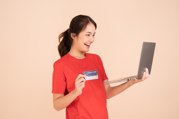 Una mujer joven con una camisa roja tiene una tarjeta de crédito y usa una computadora portátil