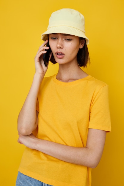 Mujer joven camiseta amarilla y sombrero estilo verano con fondo amarillo de teléfono