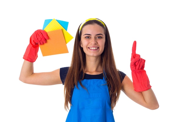 Mujer joven en camiseta azul y delantal con guantes rojos mostrando plumeros sobre fondo blanco en el estudio