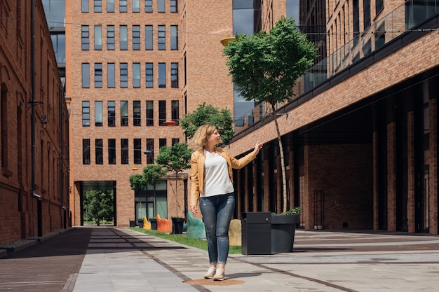 Mujer joven en camiseta blanca, chaqueta, jeans y zapatillas de deporte está completamente preparada para un largo paseo por las calles de la ciudad en primavera. Paisaje urbano . Turismo y placer. Bloguear sobre viajes.