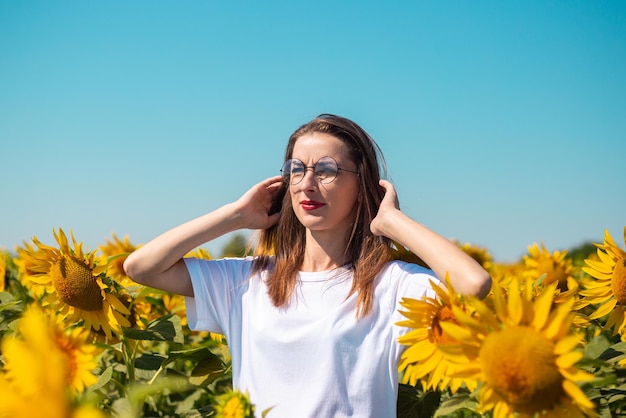 Mujer joven con camiseta blanca y gafas en un campo de girasoles en un día soleado de verano