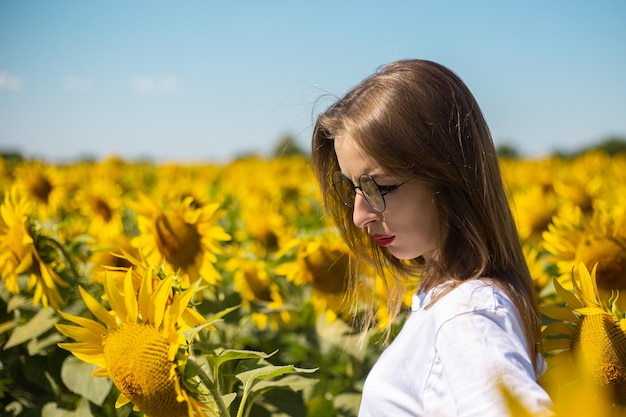Mujer joven con camiseta blanca y gafas en un campo de girasoles en un día soleado de verano