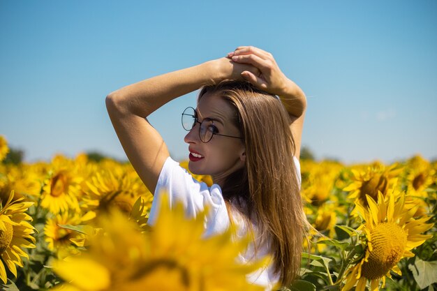 Mujer joven en camiseta blanca y gafas en un campo de girasoles en un día soleado de verano.