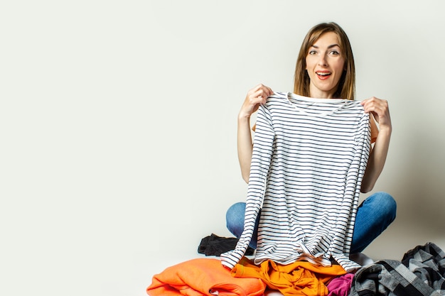 Foto mujer joven en una camiseta y jeans elige cosas de vestuario mientras está sentado en el piso