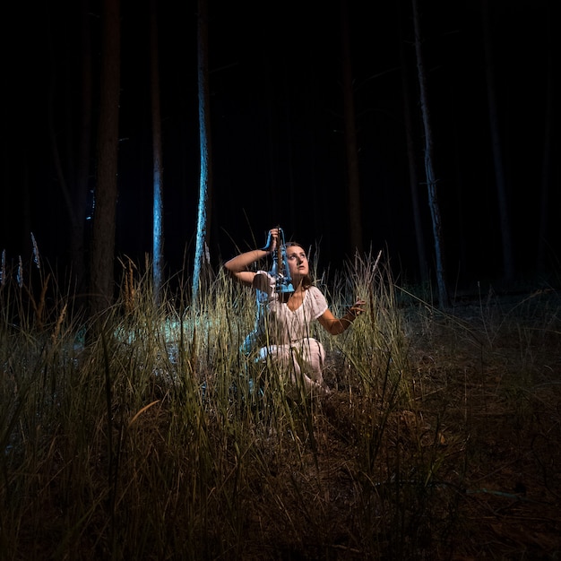 Mujer joven, en, camisón, sentado, en, bosque alto, por la noche, con, linterna