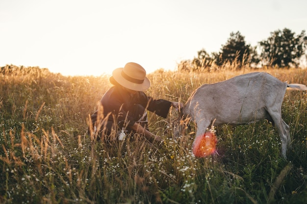 Mujer joven en el campo está pastando sus cabras blancas La niña y las cabras en el prado en verano Amor por los animales Granja de cabras Mascotas Mujer feliz con animales Amabilidad y amor por los animales Besa a una mascota