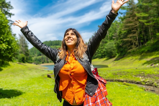 Mujer joven en un campo con un lago y un bosque de pinos