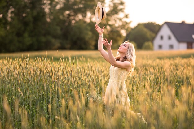 Una mujer joven en el campo lanza un sombrero.