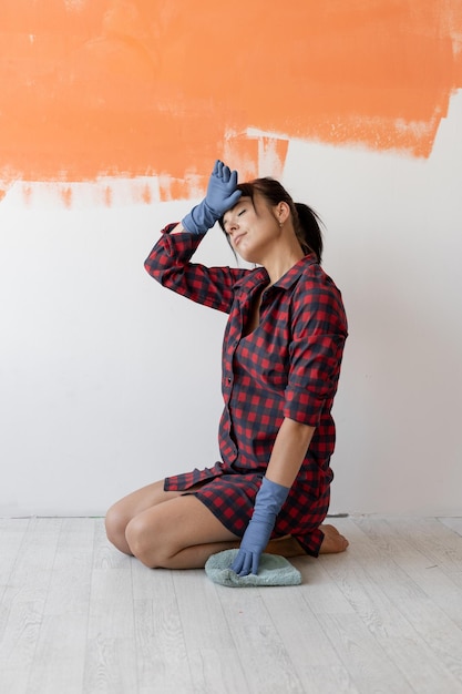 Mujer joven cansada con una camisa roja se sienta en el suelo. Lave el piso a mano con un paño de microfibra y detergente. Limpia el piso de tu frente. espacio para texto