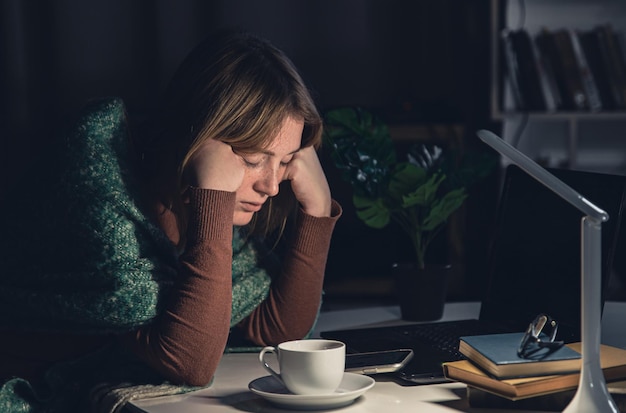 Mujer joven cansada en el lugar de trabajo quiere dormir tarde por la noche