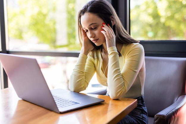 Mujer joven cansada que trabaja en la computadora portátil en su espacio de trabajo