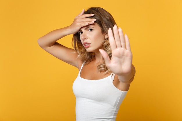 Mujer joven cansada con ropa informal ligera posando aislada en un fondo naranja amarillo en el estudio. Concepto de estilo de vida de las personas. Simulacros de espacio de copia. Mostrando gesto de parada con la palma, poniendo la mano en la frente.