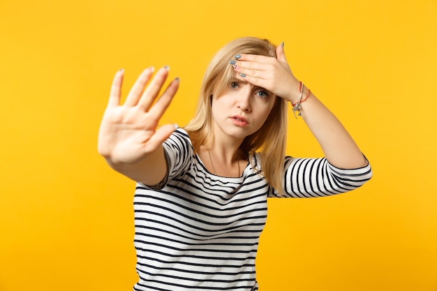 Mujer joven cansada con ropa a rayas que muestra un gesto de parada con la palma, poniendo la mano en la frente aislada en el fondo de la pared naranja amarilla. Gente emociones sinceras concepto de estilo de vida. Simulacros de espacio de copia.