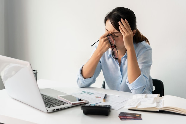 Mujer joven cansada siente dolor vista cansada sosteniendo gafas frotando los ojos irritados secos fatigados por el trabajo de la computadora portátil mujer estresada sufre de dolor de cabeza mala visión problema de vista sentarse en el lugar de trabajo