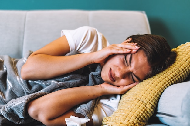 Mujer joven cansada tocando la frente con dolor de cabeza, migraña o depresión, acostado en un sofá en la sala de estar