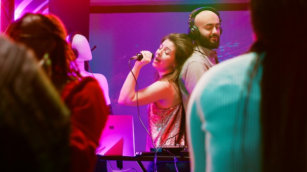 Foto mujer joven cantando canciones con dj, creando una actuación divertida en el escenario del club. persona alegre disfrutando de la noche de karaoke con un grupo de amigos, de fiesta con la gente en la discoteca moderna.