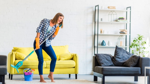 Foto mujer joven cantando con un trapeador mientras limpiaba la habitación