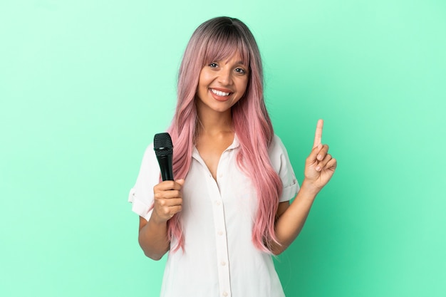 Mujer joven cantante de raza mixta con cabello rosado aislado sobre fondo verde apuntando hacia una gran idea